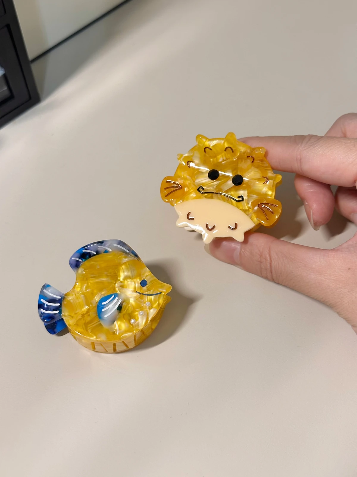 手拿黃色河豚款鼓鼓河豚與熱帶魚小髮夾，旁邊是黃藍熱帶魚款
